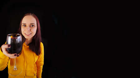 Relaxed young woman poses with glass of red wine on black background. Adult happy brunette resting with alcohol in her weekendの写真素材