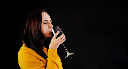 Relaxed young woman poses with glass of red wine on black background. Adult happy brunette resting with alcohol in her weekendの写真素材