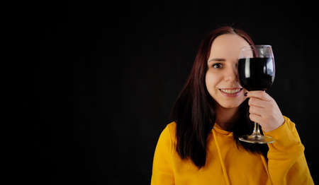 Relaxed young woman poses with glass of red wine on black background. Adult happy brunette resting with alcohol in her weekendの写真素材