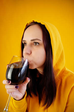 Relaxed young woman poses with glass of red wine on yellow background. Adult happy brunette resting with alcohol in her weekendの写真素材