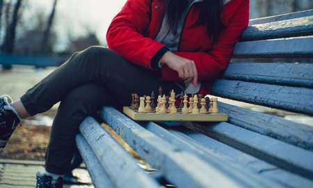 Close up of chess on wooden bench. Body part of unrecognizable woman playing in board game in city parkの写真素材