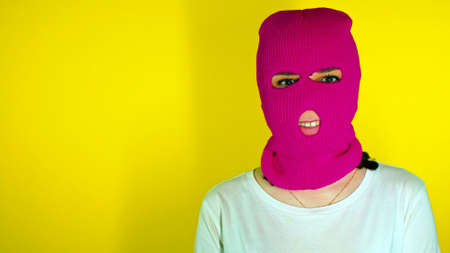 Unrecognizable woman in pink balaclava smiles on yellow background. Unknown female in mask smiling and looking at cameraの写真素材