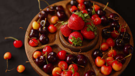 menazhnitsa with red strawberries and cherries on a dark background. Wooden plate made with...