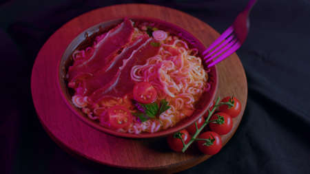 Close up of ready-made instant noodles with cherry tomatoes and dried meat in plate on tray....