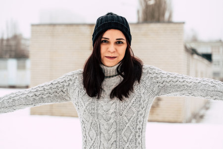 Young, beautiful woman with winter cap and gray sweater standing outside in winter