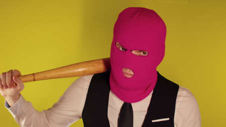 Man in pink balaclava with baseball bat. Hooligan in mask with bat in hands. A man in a business strict elegant suit with a wooden bat in his handsの写真素材