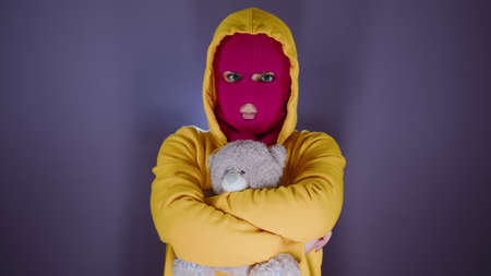 Young woman in pink balaclava with teddy bear. Hooligan in mask with plush toy in hands.