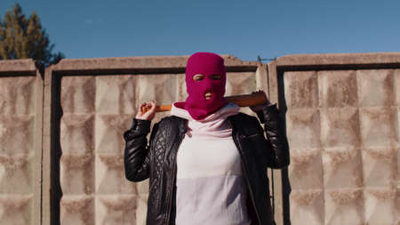 Young woman in pink balaclava with baseball bat. Hooligan in mask with bat in hands.の写真素材