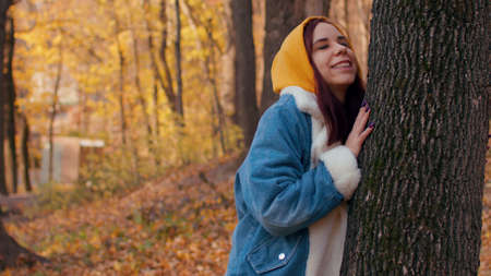 Young woman hugs tree in autumn forest. Beautiful female hugs tenderly trunk of tree in autumn season.の写真素材