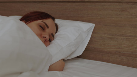 Young woman under blanket sleeping on bed in morning. Sleepy female wakes up and yawns, lying on pillow.の写真素材