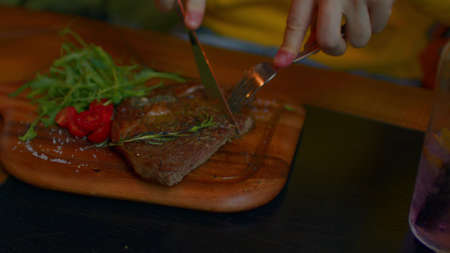 Succulent steak with vegetables on wooden board. Unrecognizable man cuts off piece and eats. Food...