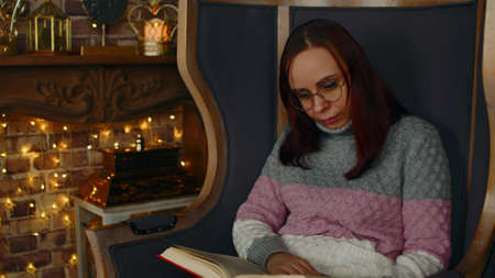 Young woman in glasses reading book. Interested student in eyeglasses reads book, preparing for educational lessons.の写真素材