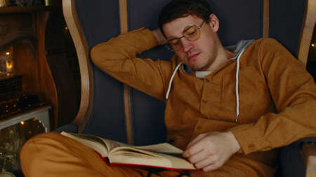 Young man in glasses reading book. Interested student in eyeglasses reads book, preparing for...