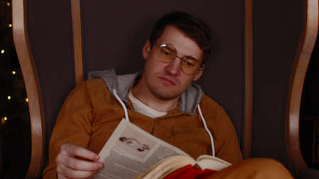 Young man in glasses reading book. Interested student in eyeglasses reads book, preparing for...