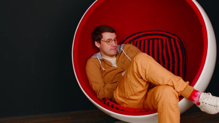 Young man with mobile phone sitting in ball chair on black background. Male browsing smartphone and...