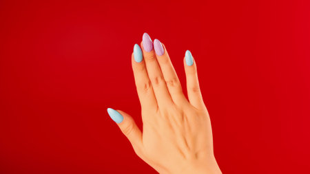 Womans hand with beautiful nails on red background. Unrecognizable person shows manicure. Close up....