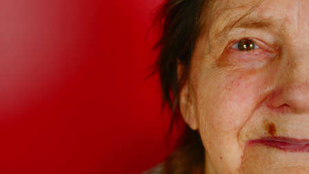 Part of elderly womans face on red background with space for text. Mature woman smiling and looking...