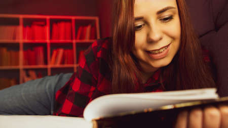 A beautiful student reading a big book. A thoughtful young woman lying on the sofa with a book and...