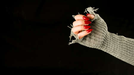 Womans hand with red nails on black background. Unrecognizable woman in stylish knitted gloves showing manicure. Concept of care and beauty.の写真素材