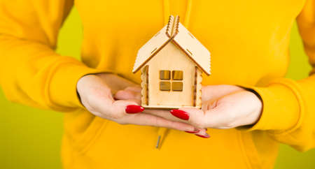 Body part of woman with small wooden house in hands. Crop unrecognizable person holding small toy house. Concept of purchasing new apartment and roof overhead.の写真素材