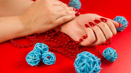 From above of crop anonymous woman with red beads and with red manicure on red background in studio with decorative wicker ballsの写真素材