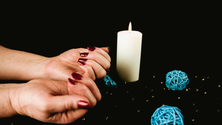 Crop woman with burning candle. Crop anonymous person demonstrating burning candle with red manicure against black backgroundの写真素材
