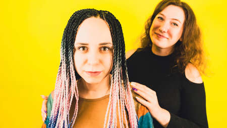 Young women looking at camera. One female standing in front, other behind and hugs her shoulders.