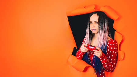 Smiling woman with gamepad and playing video game. A stylish girl gamer in a bright red dress...