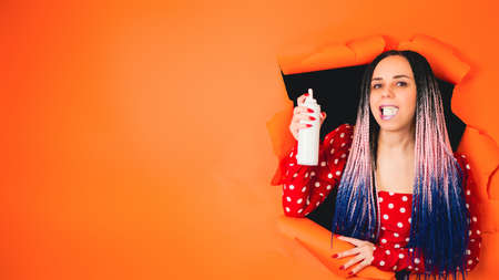 Beautiful woman looking at camera while eating whipped cream from bottle. A stylish girl in a bright red dress eating whipped cream from bottleの写真素材