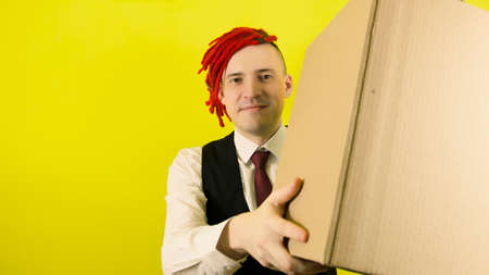 Young man in white shirt, vest and tie with cardboard box on yellow background in studio. Male...