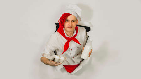 Man with red dreadlocks holds it in his hand chicken eggs and milk. Confident young cook in white...