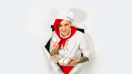 A handsome man with red dreadlocks holds it in his hand chicken eggs. Confident young cook in white...