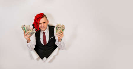 Happy young man with red dreadlocks waving dollar bills. Stylish hipster rejoicing in money through...