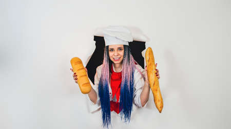 Young woman dressed as chef holding white bread. Female cook with loaf in hole of white background.の写真素材