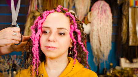 Unrecognizable person makes curly hairstyle for young woman in salon. Professional hairstylist makes pink and brown dreadlocks for clientの写真素材