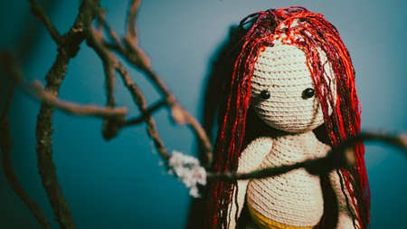 Knitted doll with dreadlocks hanging on wall. Handmade soft toy with hairstyle on blue wall. Concept of interior and beautyの写真素材