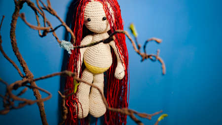 Knitted doll with dreadlocks hanging on wall. Handmade soft toy with hairstyle on blue wall. Concept of interior and beautyの写真素材