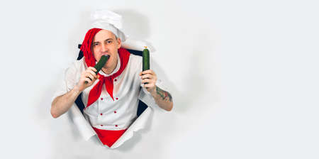 Crazy male cook with vegetables sticking out of hole of white background.の写真素材