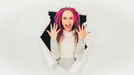 Young woman showing manicure in hole of white background. Beautiful female with curly hair showing...