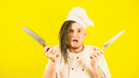 Crazy male cook in white hat and shirt posing with kitchen knives.の写真素材