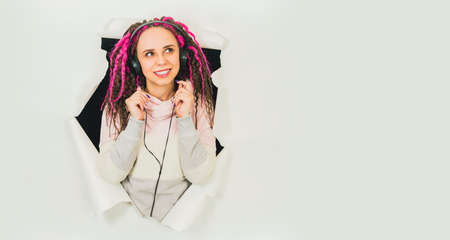 Young woman in headphones in hole of white background. Beautiful female with curly hair listening to music in studioの写真素材