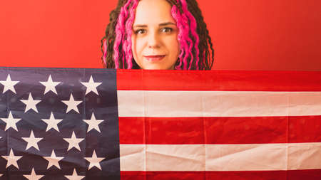 Young woman with American flag on red background. Happy female smiling and looking at camera, holding American flagの写真素材