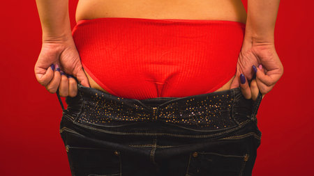 Back body part of young female in red underwear. Unrecognizable woman trying to pull on small jeans on buttocks. concept of overweight, obesityの写真素材