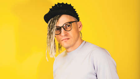 Young handsome man in glasses, in black cap on yellow background. Hipster looking at camera with blonde dreadlocks.の写真素材