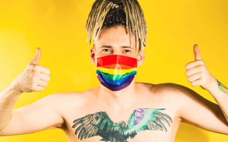handsome young man in LGBT mask showing gesture of like. Attractive gay guy with blonde dreadlocks...