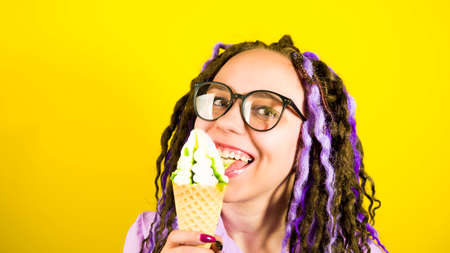 Young woman in glasses licking ice cream, smiling, looking at camera. Cheerful female with...
