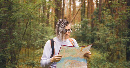 Traveling man with dreadlocks with map in woods. Male traveler with backpack in woods reading map in...