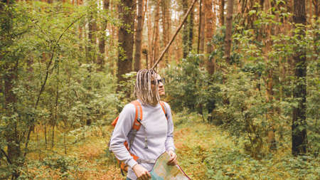 A traveling man with dreadlocks with a map in the forest. A male traveler with a backpack and a map...