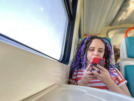 Young relaxed woman riding on train, browsing mobile phone. Concentrated female using smartphone,...