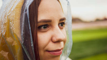 Young woman in raincoat in rainy weather. Portrait of female in wet waterproof coat. close upの写真素材